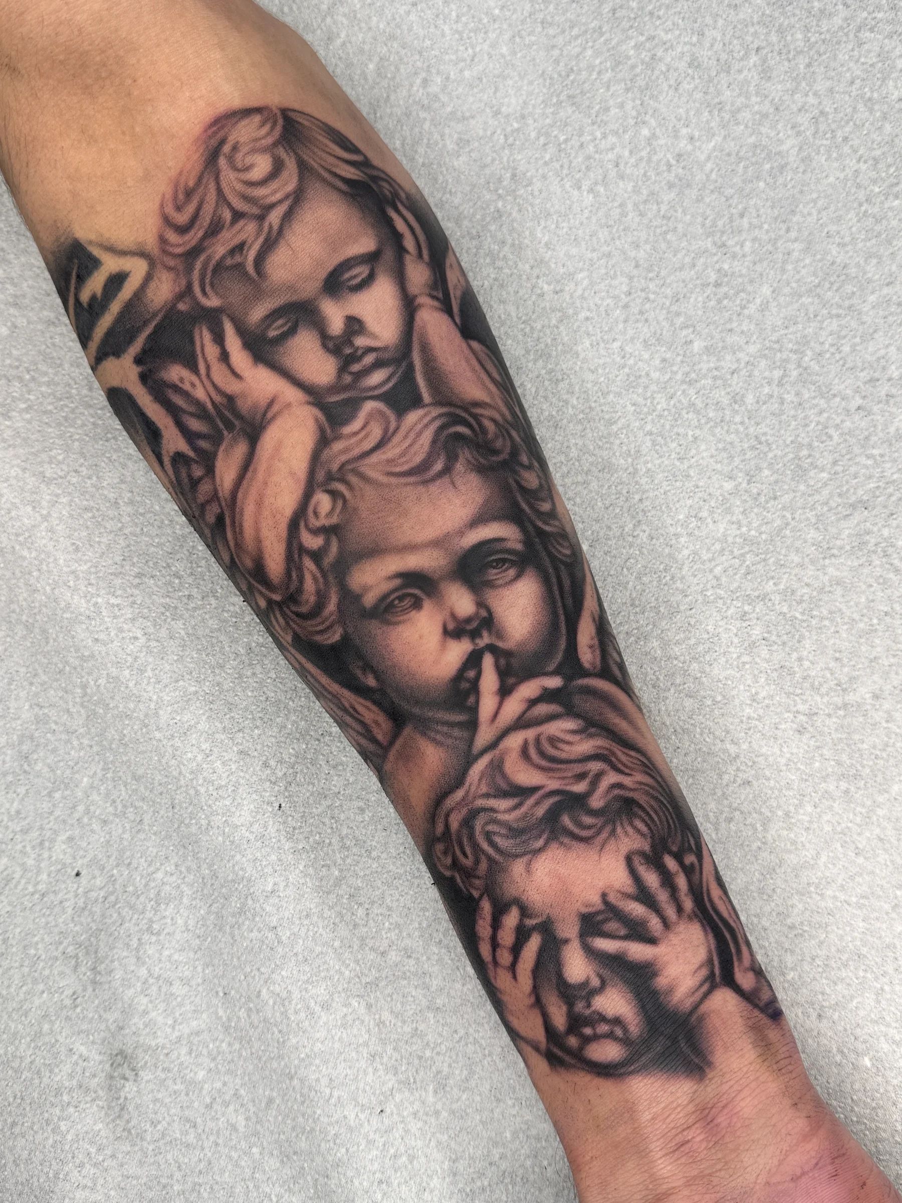 Three cherubs covering their eyes, mouth and ears, on the forearm