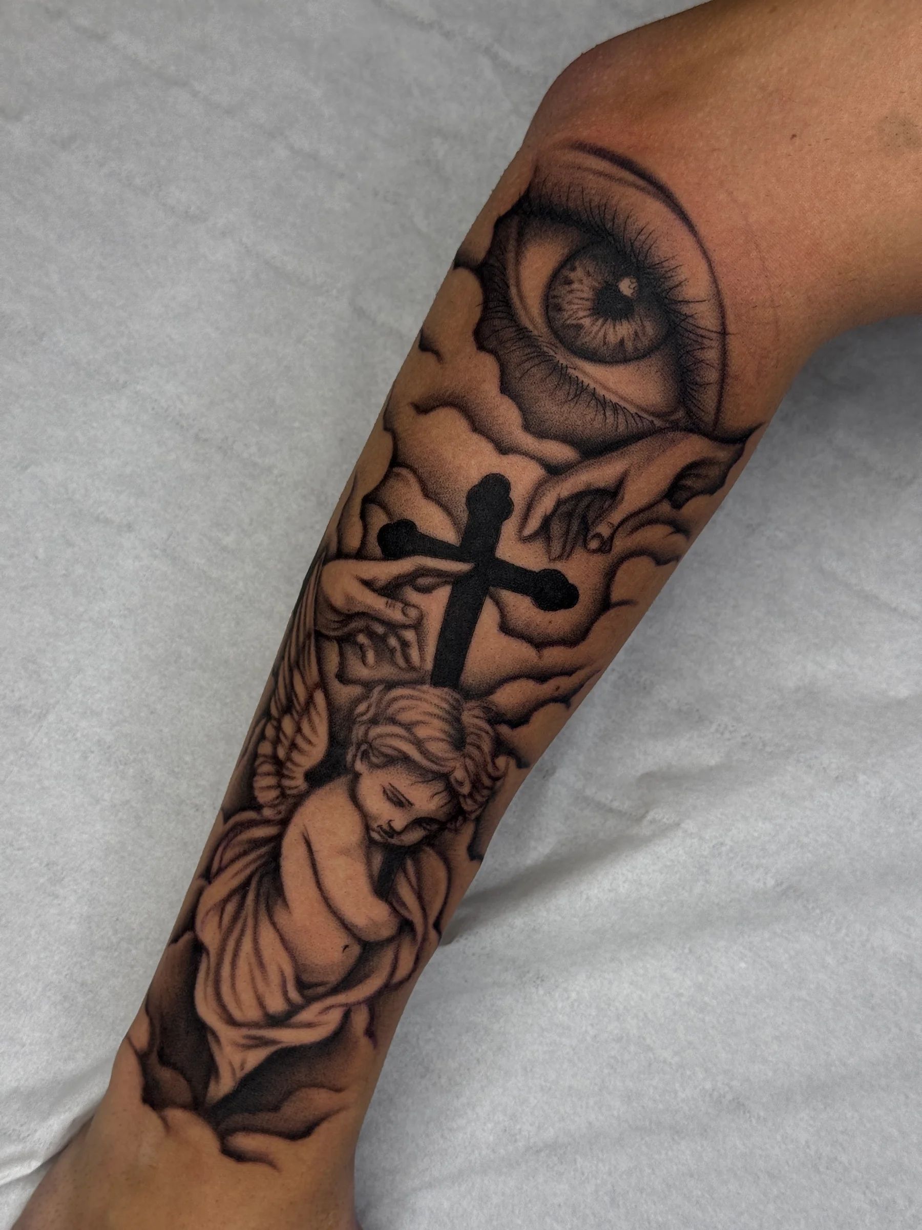 An eye among clouds, a cross and a cherub on the forearm