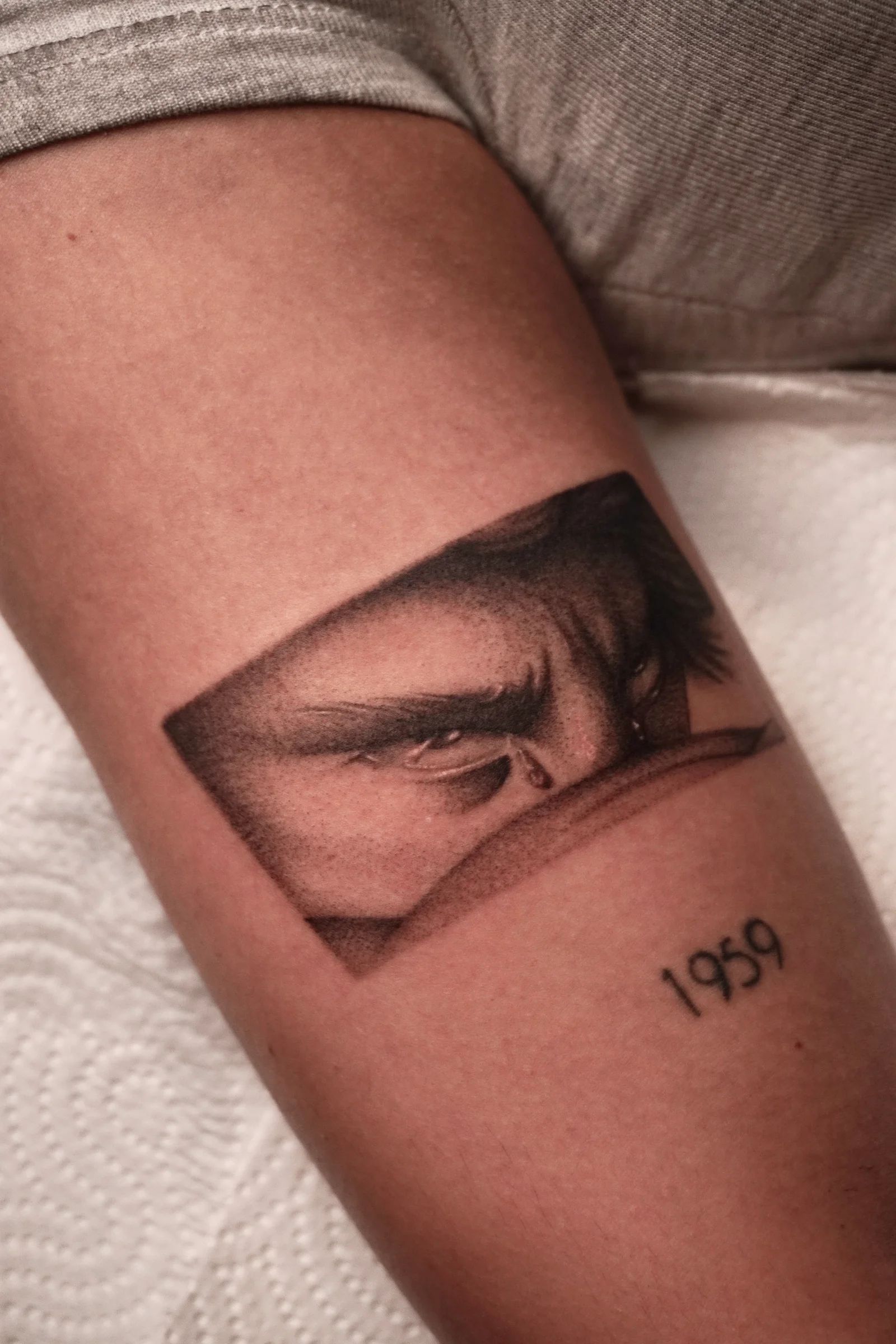 A pair of eyes in a frame with the year 1959, on the forearm