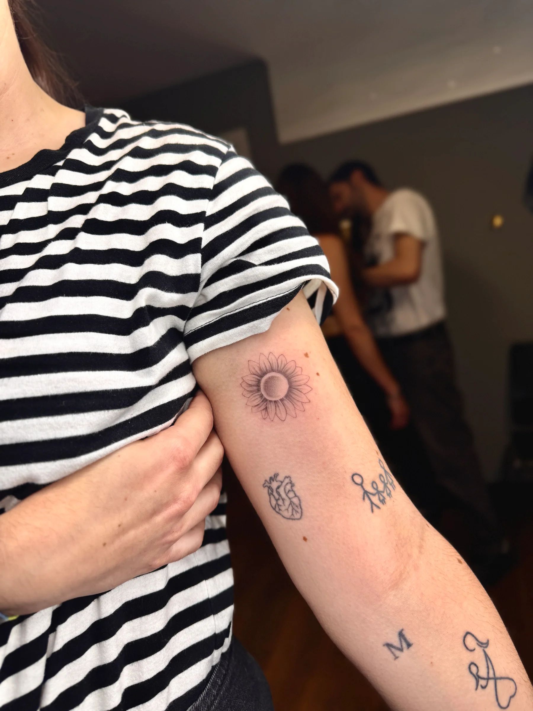 Several small tattoos on the arm: a sun, a heart and letters